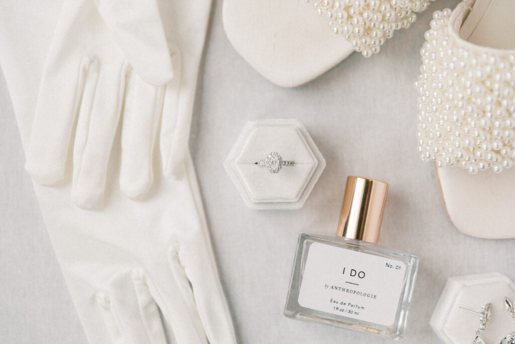 bride detail flatlay photo with ring, gloves, perfume, and shoes 
