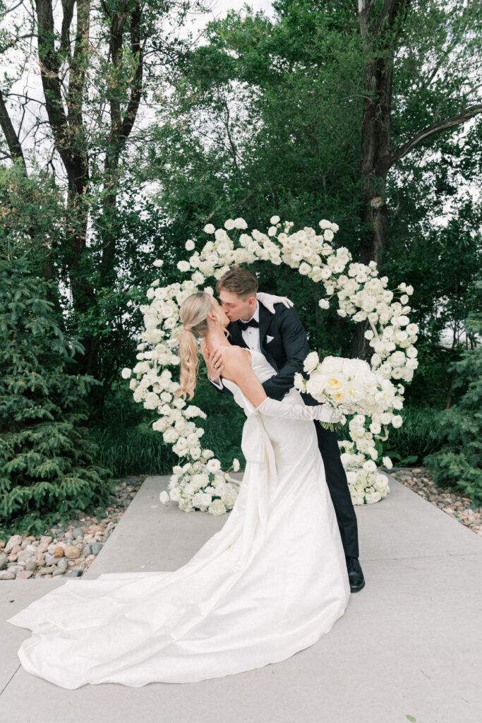 bride and groom kissing at the alter with floral arch behind them 