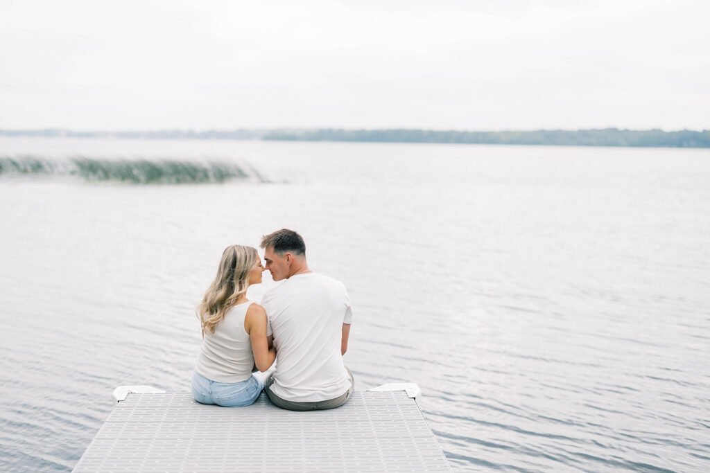 engagement session location idea, couple sitting on a dock in front of a lake 