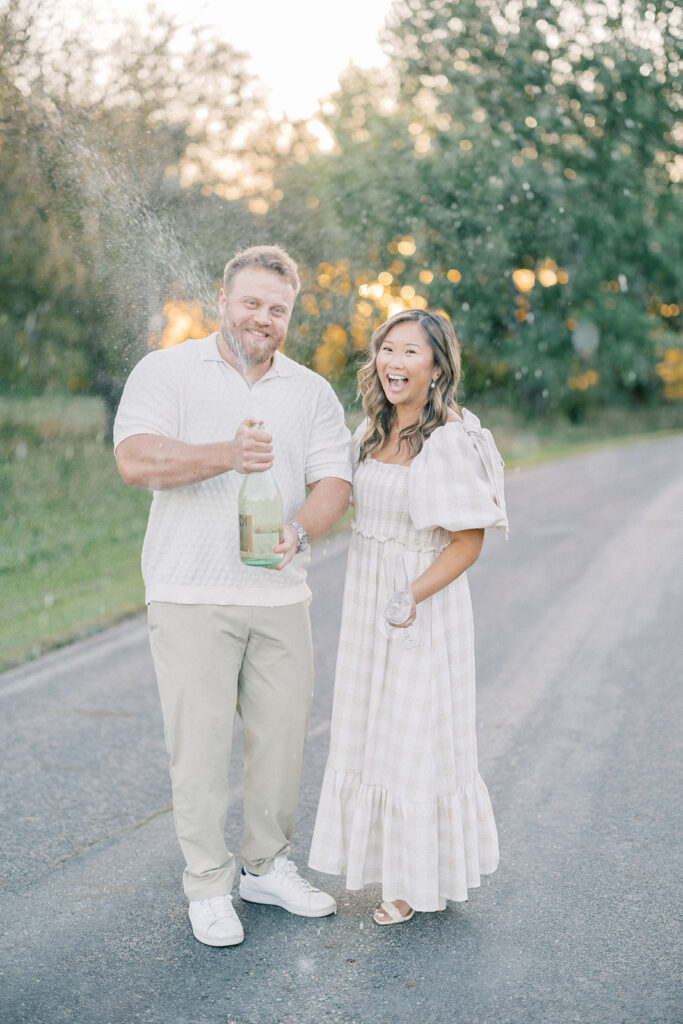 engagement session, a couple popping a bottle of champagne on a road surrounded by greenery