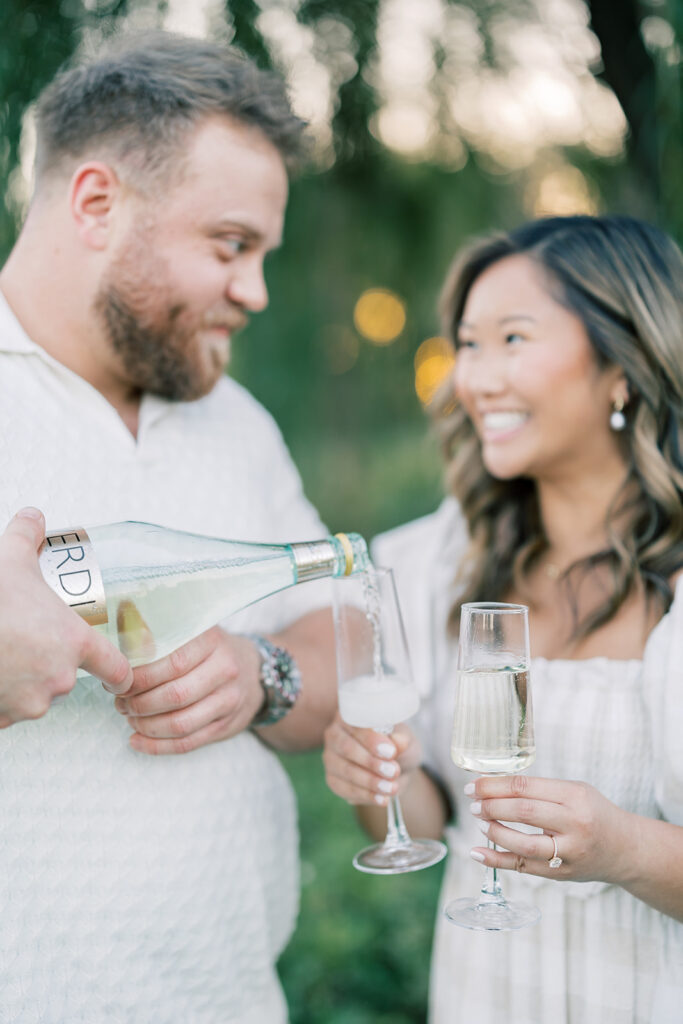 engagement session, a couple pouring champagne on a road surrounded by greenery