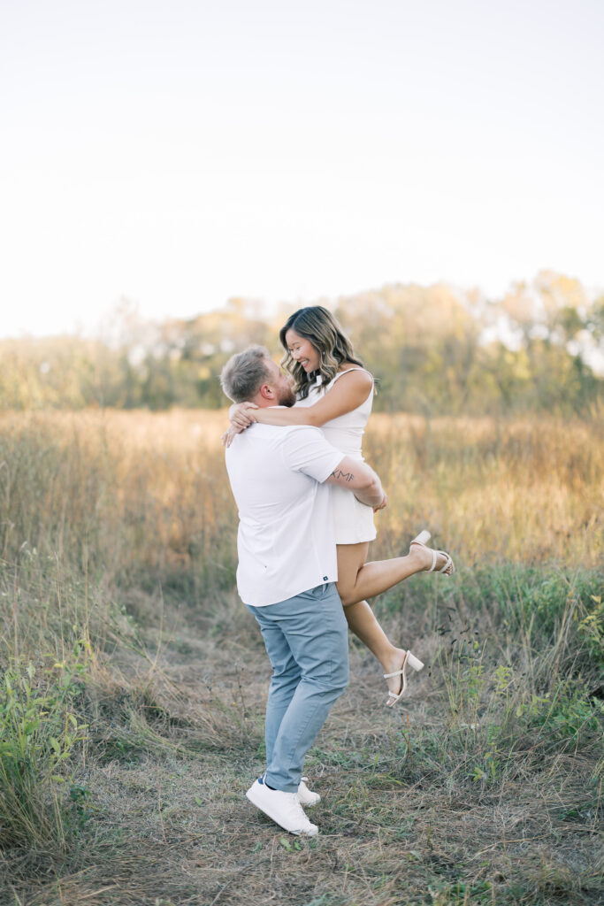 engagement session, a couple embracing in a field surrounded by greenery
