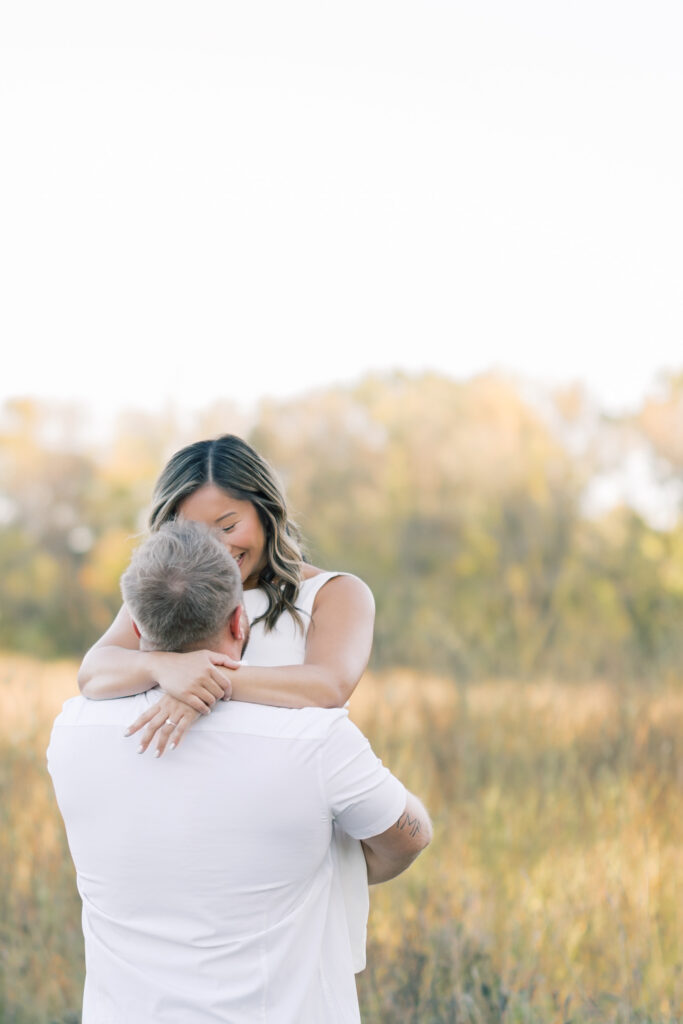 engagement session, a couple embracing in a field surrounded by greenery