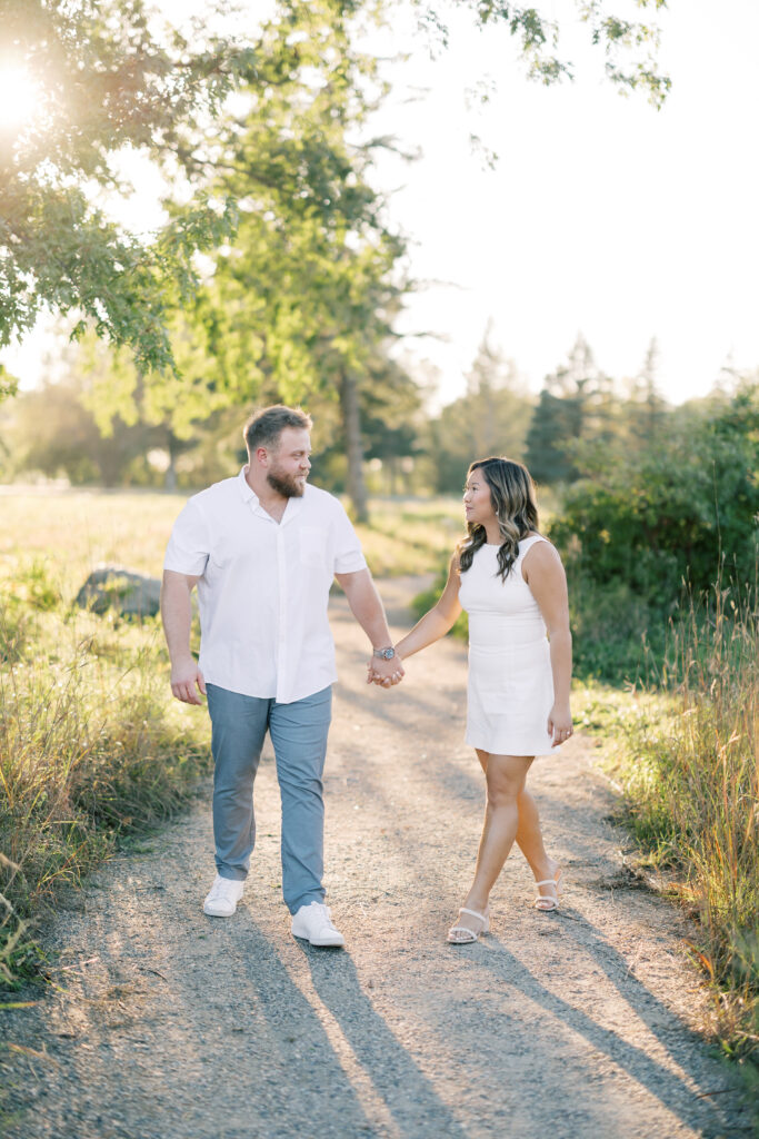 engagement session, couple walking down a sunlit path surrounded by greenery