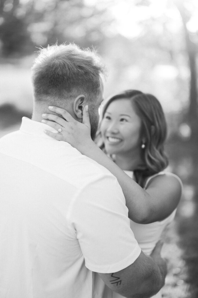 engagement session, a black & white photo of a couple embracing in a field surrounded by greenery