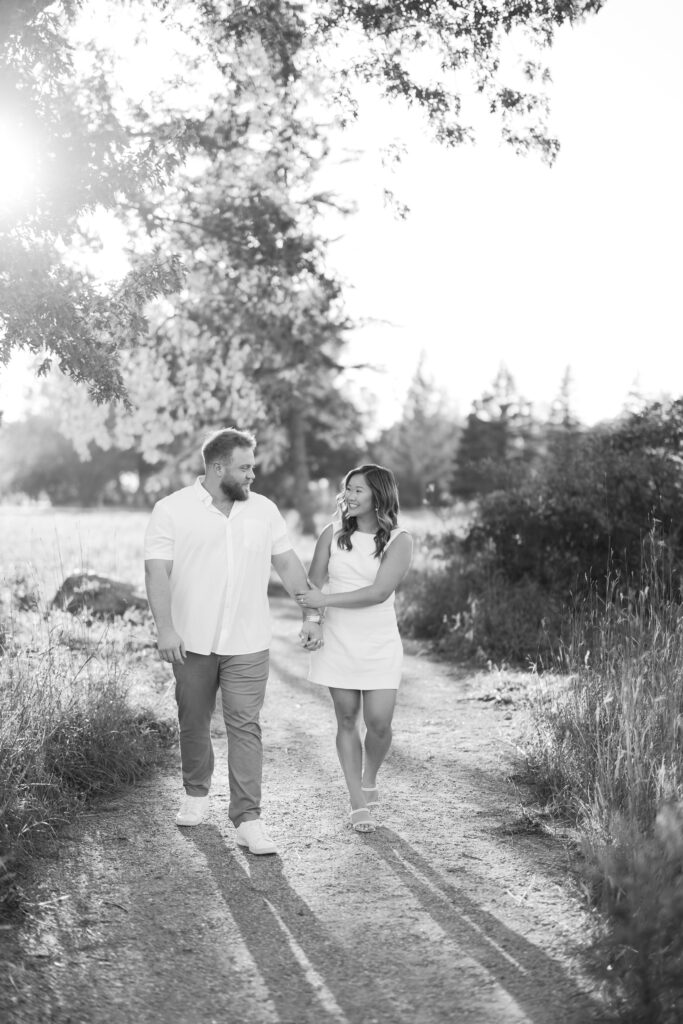 engagement session, black & white photo of a couple walking down a sunlit path surrounded by greenery
