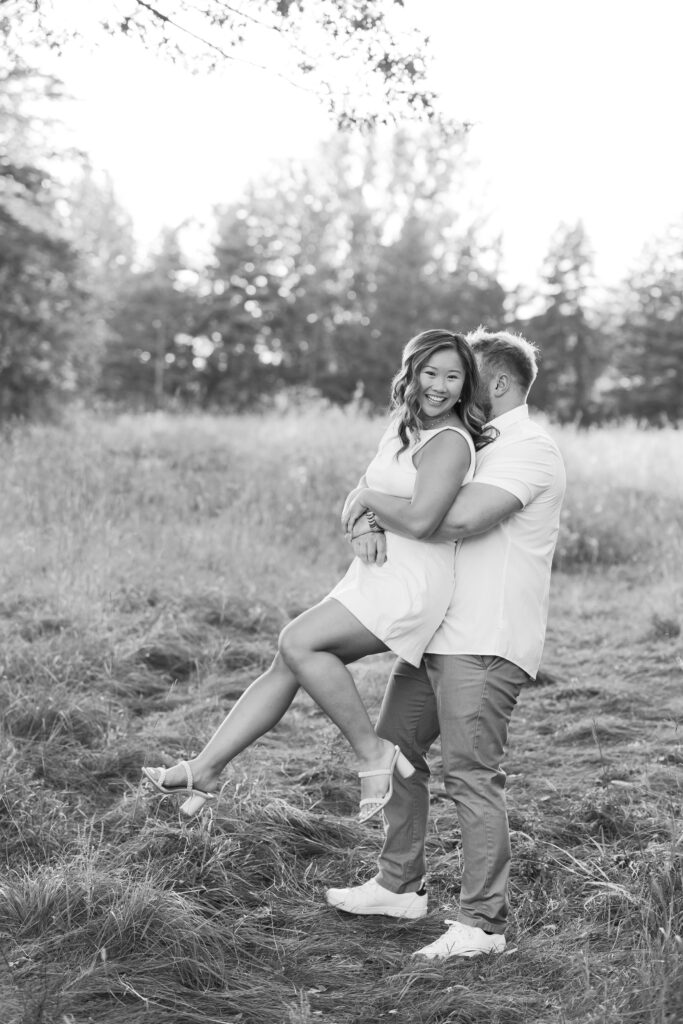 engagement session, a black & white photo of a couple embracing in a field surrounded by greenery