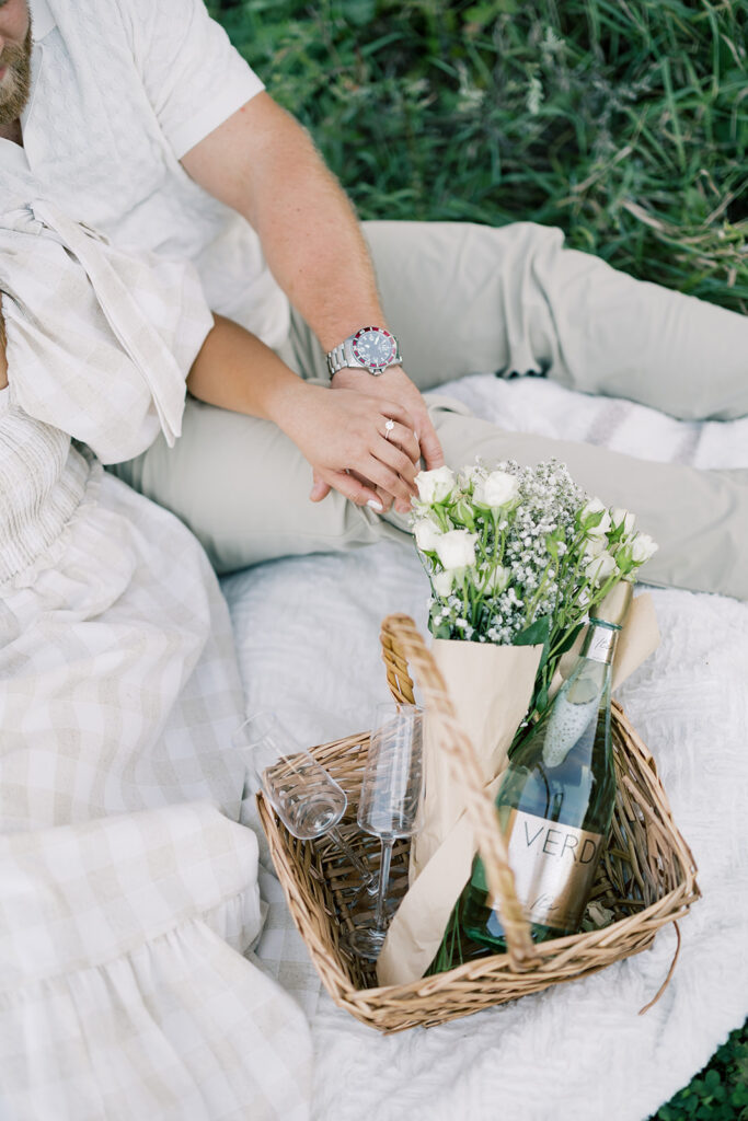 engagement session, a couple sitting on a picnic blanket in a green field with a basket full of flowers