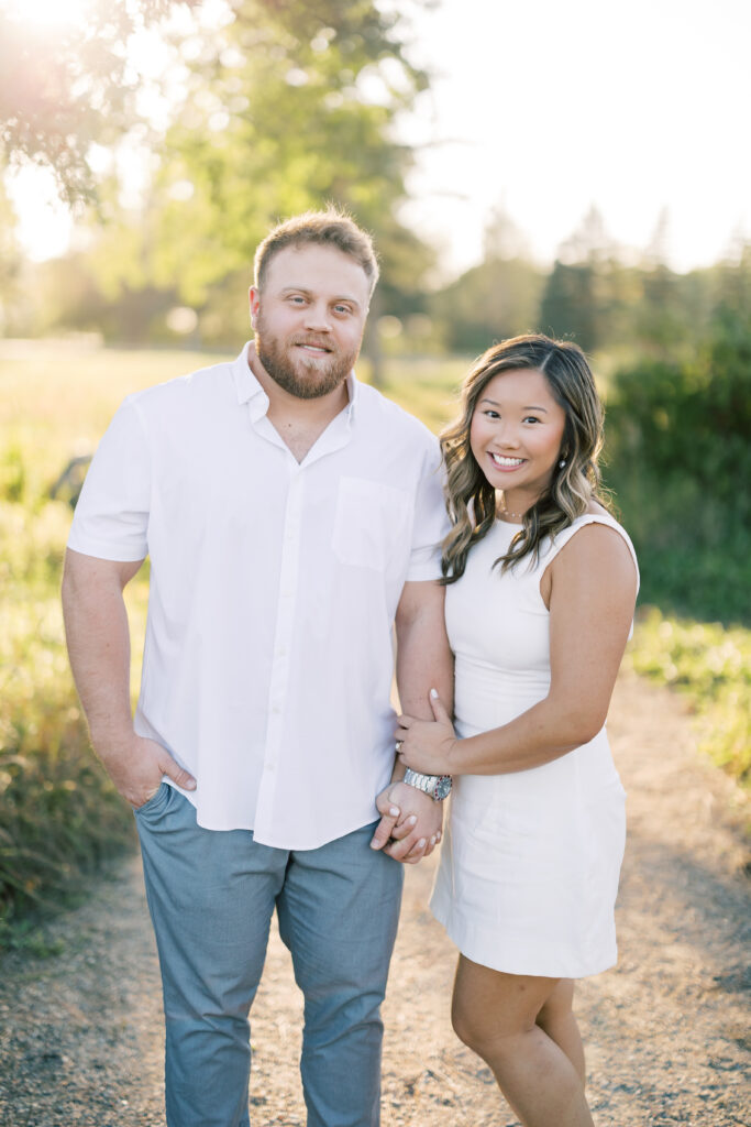 engagement session, a couple posing on a sunlit path surrounded by greenery